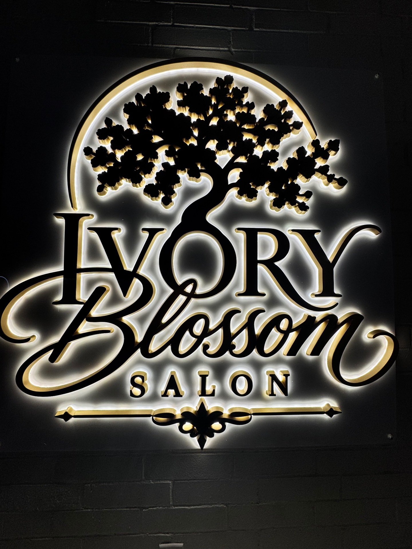 Illuminated Ivory Blossom Salon logo installed on a dark brick wall